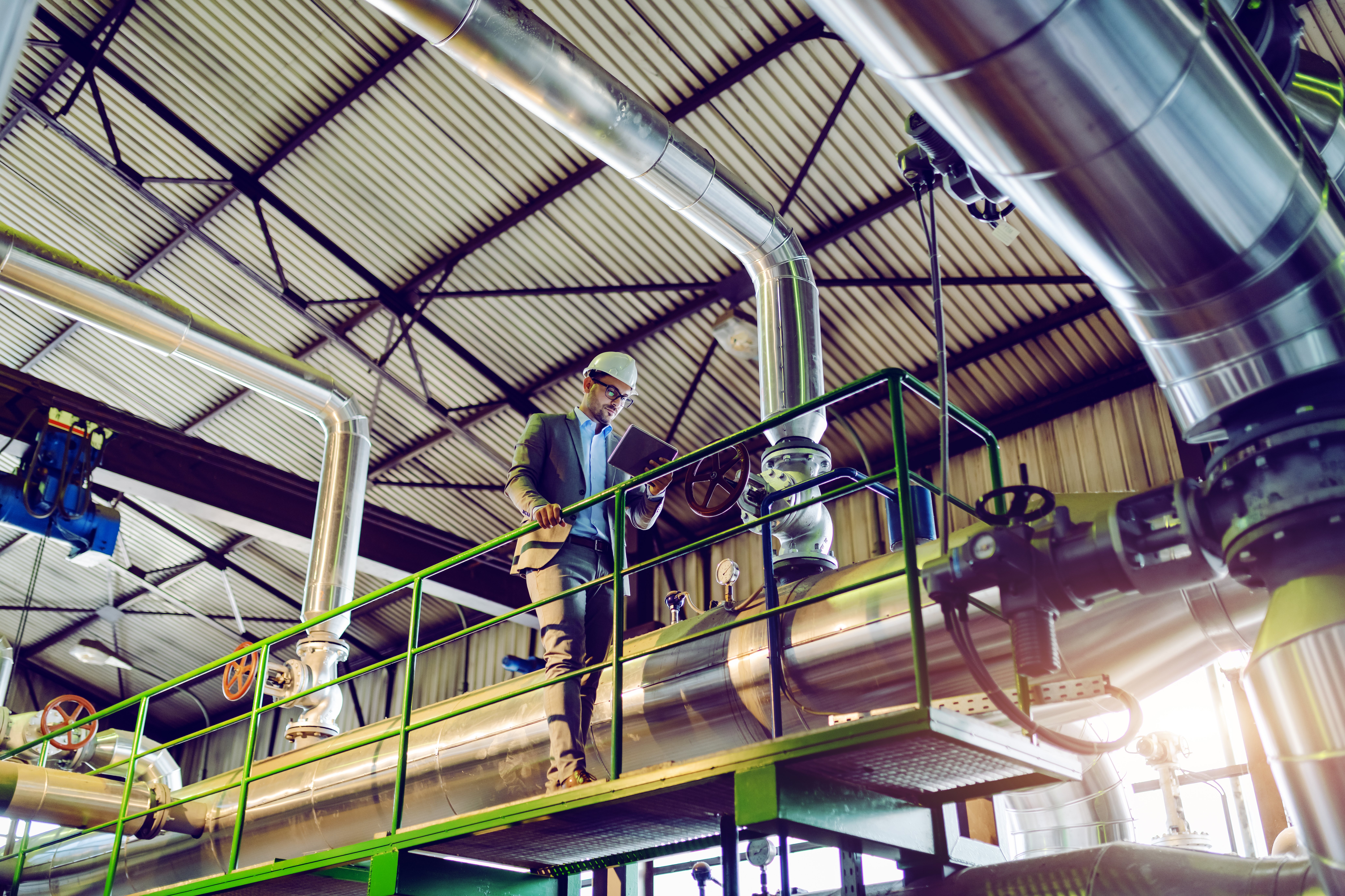 full-length-handsome-caucasian-supervisor-suit-with-helmet-using-tablet-while-leaning-railing-power-plant-interior
